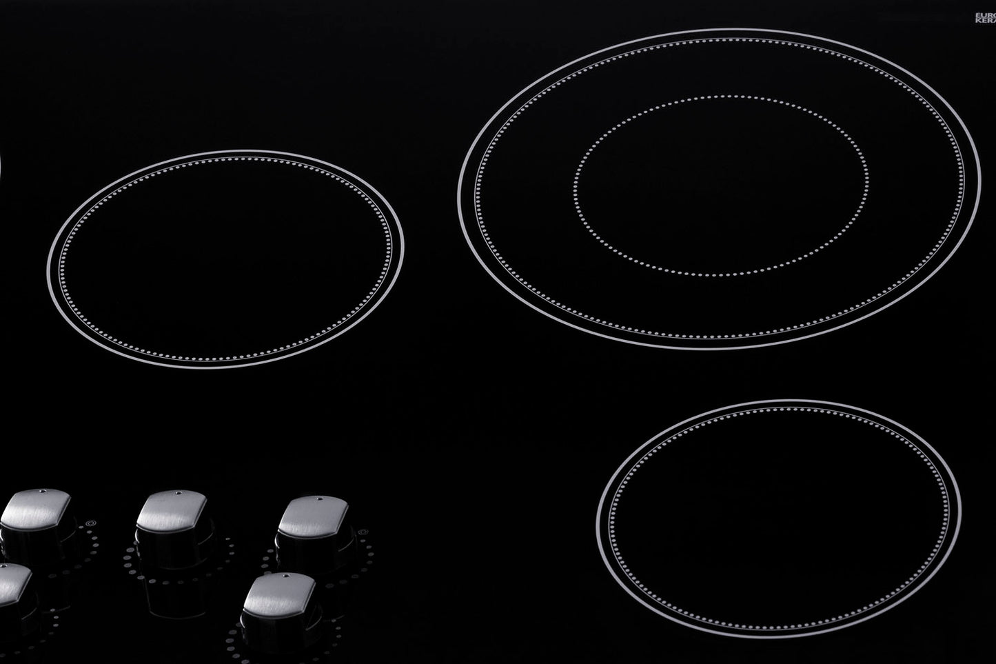 Black smooth glass radiant cooktop with five burners and four metallic control knobs from kitchen appliances collection