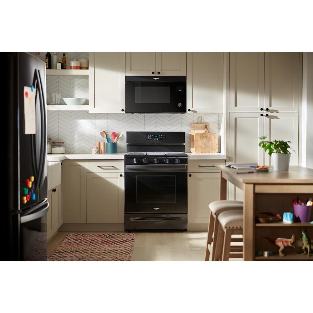 Black gas range with digital controls in a bright kitchen featuring light cabinetry and a wooden island in home appliances collection