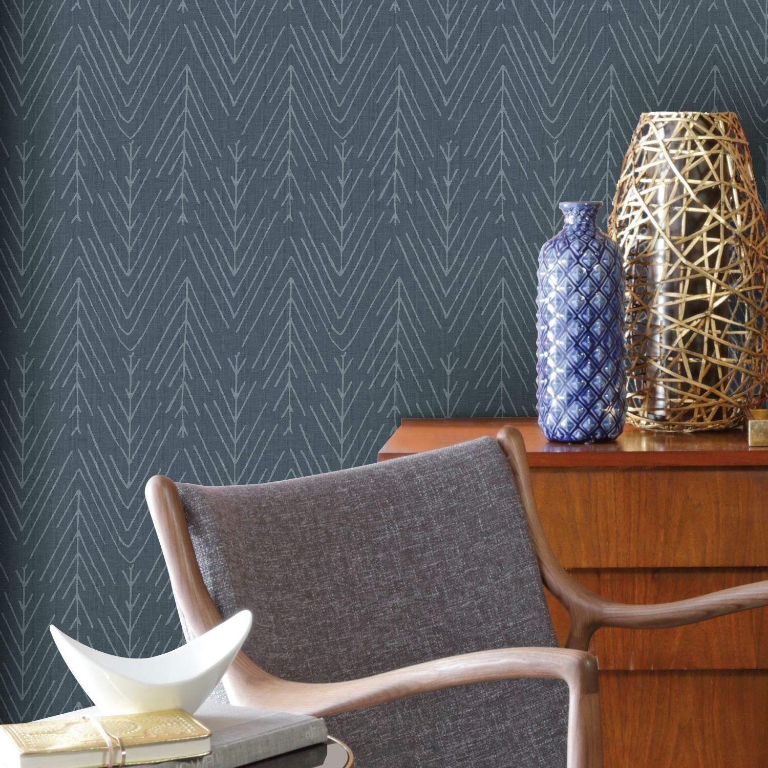 Navy wallpaper with delicate twig and herringbone pattern behind mid-century modern chair and wooden dresser decor