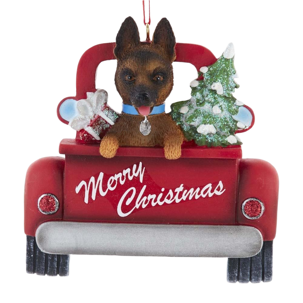 Christmas decoration showing a German Shepherd in a red truck with gifts and a snow-covered tree on the back