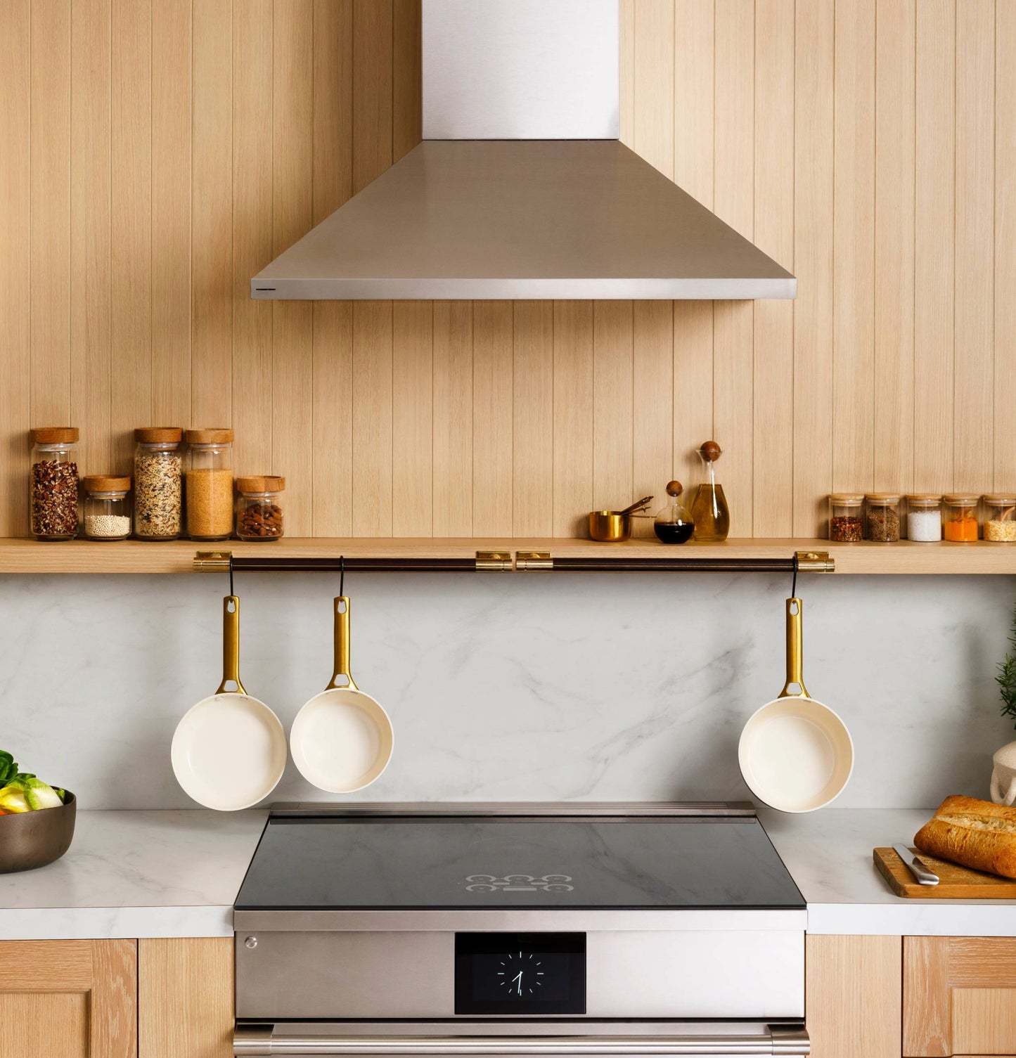 Stainless steel wall-mounted pyramid chimney vent hood with air quality sensors above modern kitchen cooktop and utensils