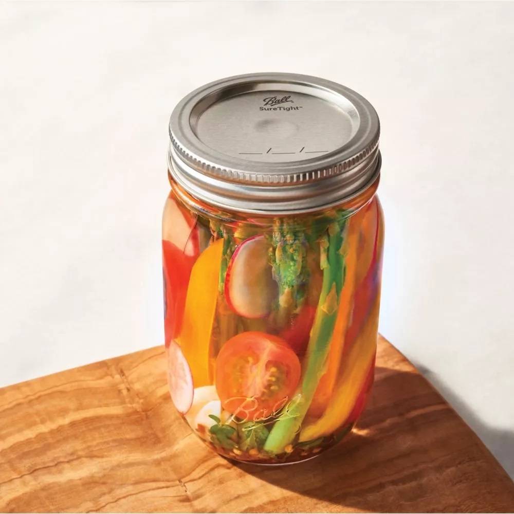 Silver-toned metal dome lid with Ball SureTight logo sealed on glass jar filled with pickled vegetables