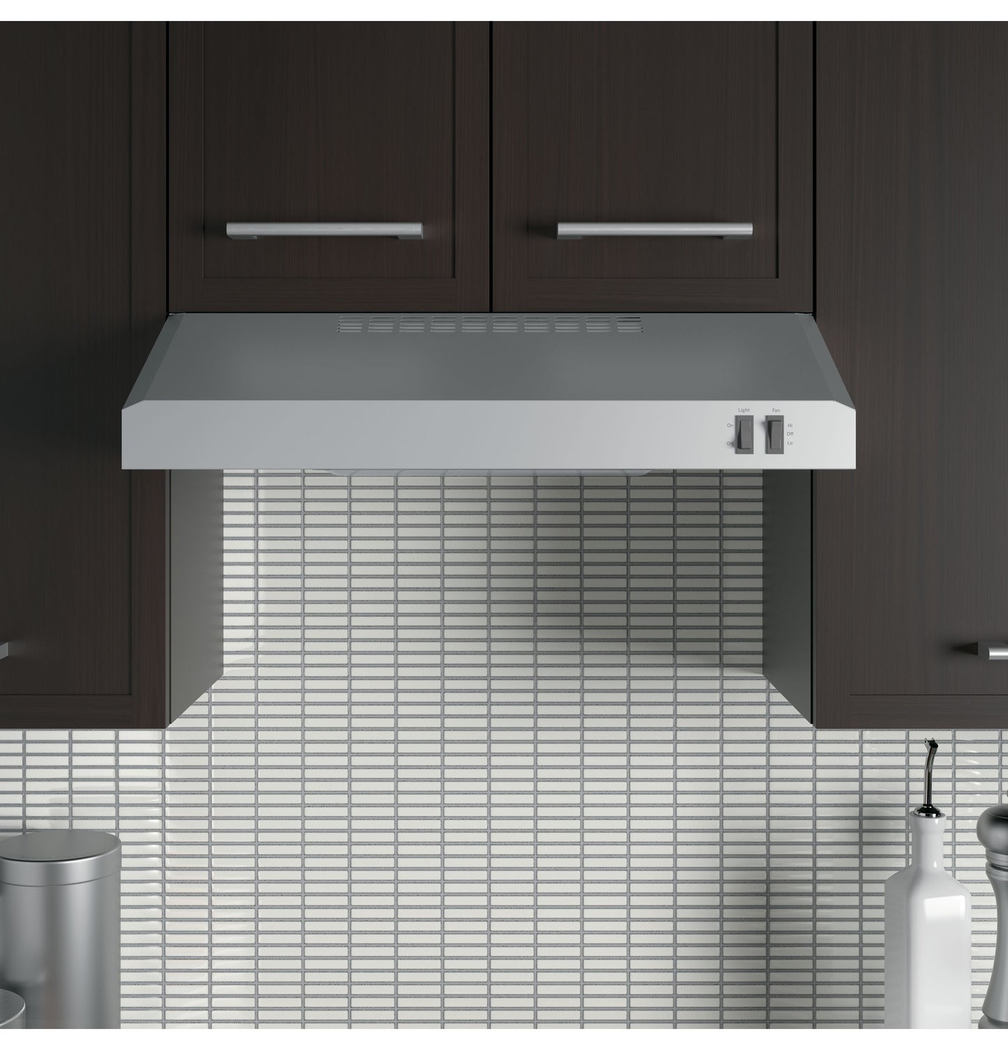 Under cabinet stainless steel range hood with manual controls installed between dark kitchen cabinets above tiled backsplash