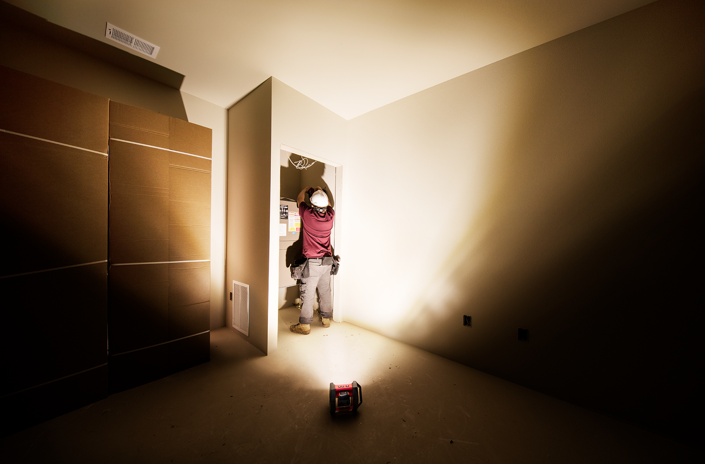 Compact red Milwaukee work light casting bright light on electrician working inside wall panel in dark room