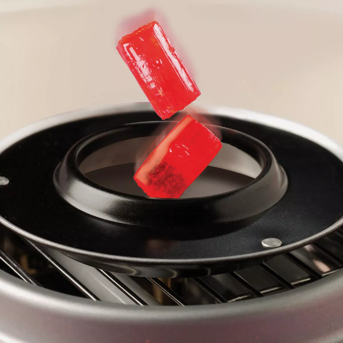 Close-up of heated extractor head with red sugar-free candy pieces melting in a small kitchen appliance setting