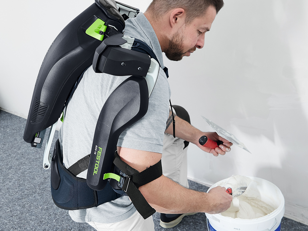 Worker wearing Festool supportive exoskeleton while applying drywall compound for home improvement tool accessories