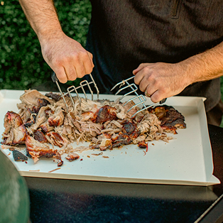 Hands shredding grilled meat on a large coated disposable cutting board for grilling and outdoor living under $50