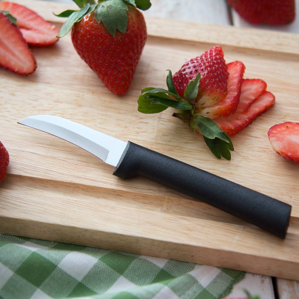 Curved paring knife with stainless steel blade and black handle on wooden cutting board with sliced strawberries in kitchenware collection
