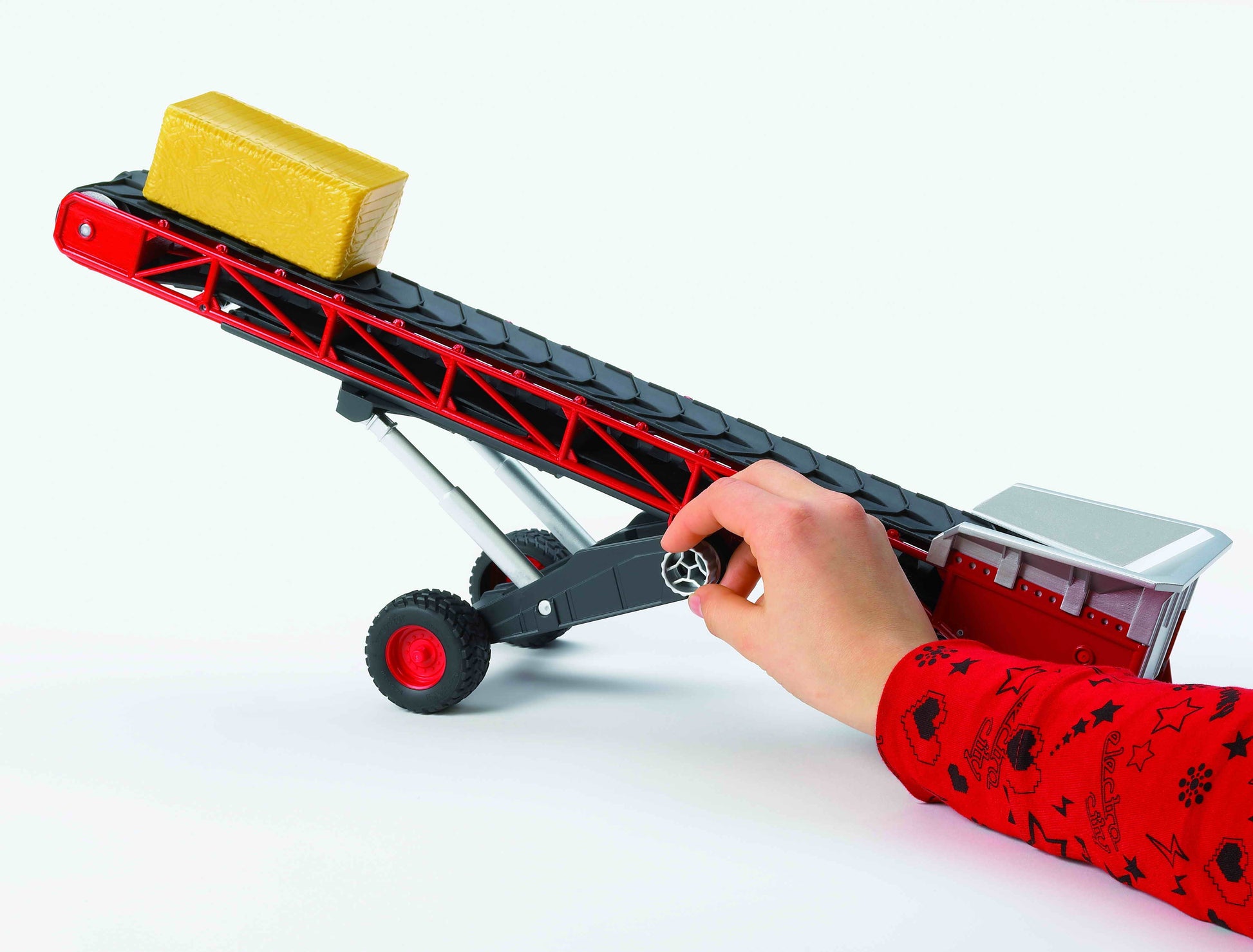 Child's hand turning crank on red and black toy conveyor belt with yellow bale in Toys & Games and Bruder collections