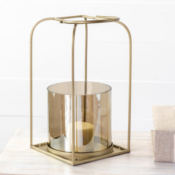 Gold metal lantern with cylindrical glass holder and candle inside on wooden surface