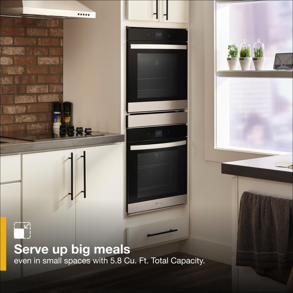 Modern stainless steel double wall oven installed in a bright kitchen with white cabinetry and brick accent wall