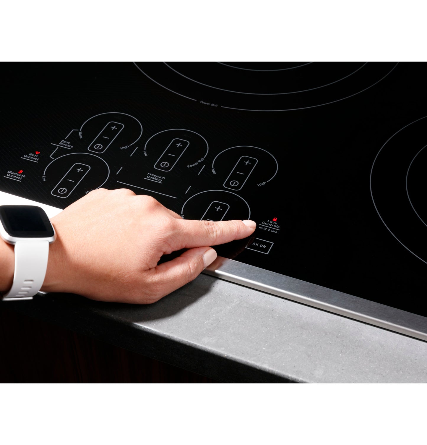 Hand pressing touch control panel on black electric cooktop set in kitchen countertop surface.
