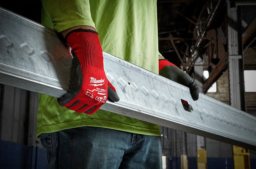 Person wearing red and black nitrile dipped gloves handling metal beam in an industrial workspace for safety and work tasks