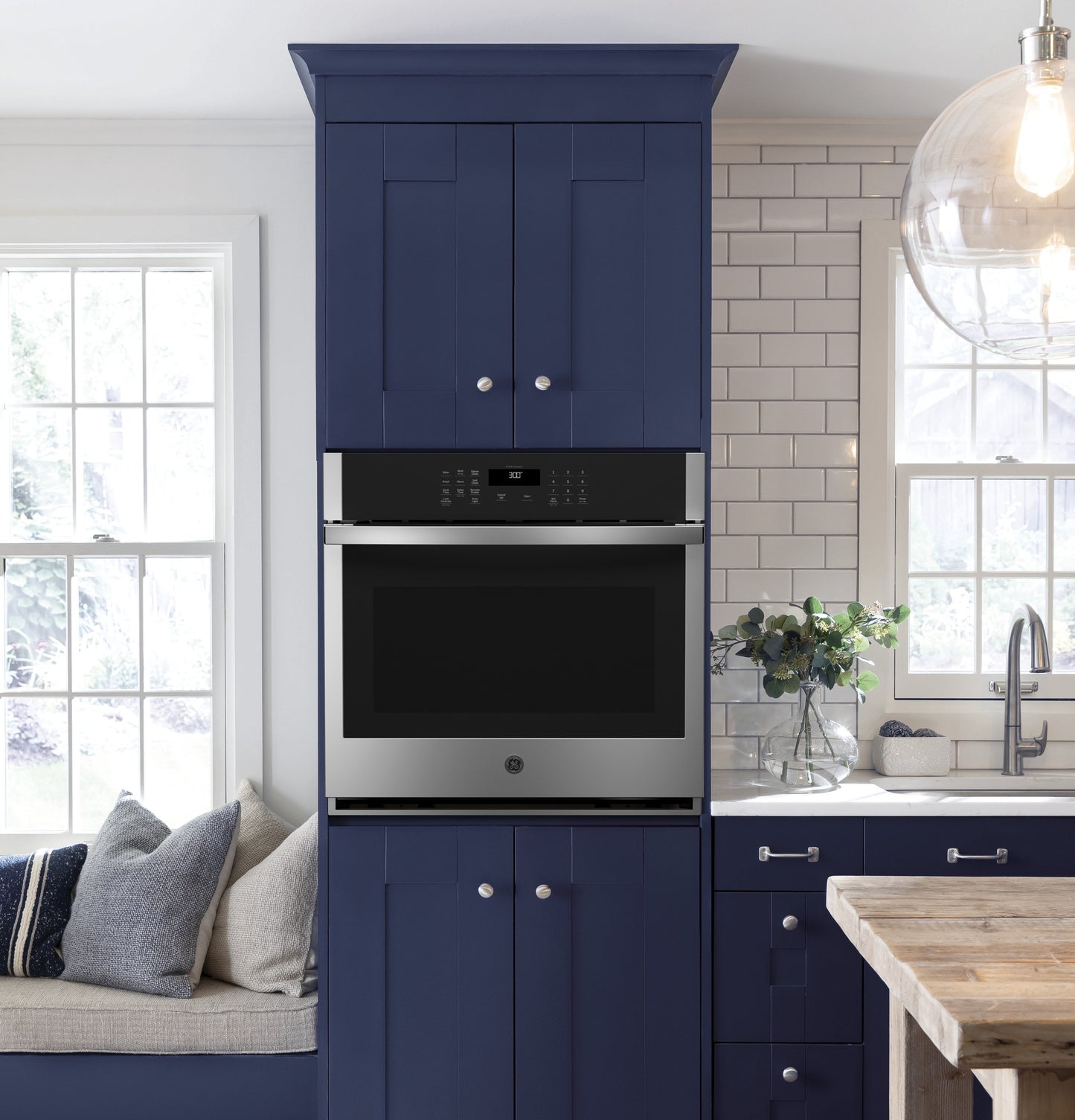 Built-in stainless steel single wall oven installed in blue kitchen cabinetry with white subway tile backsplash