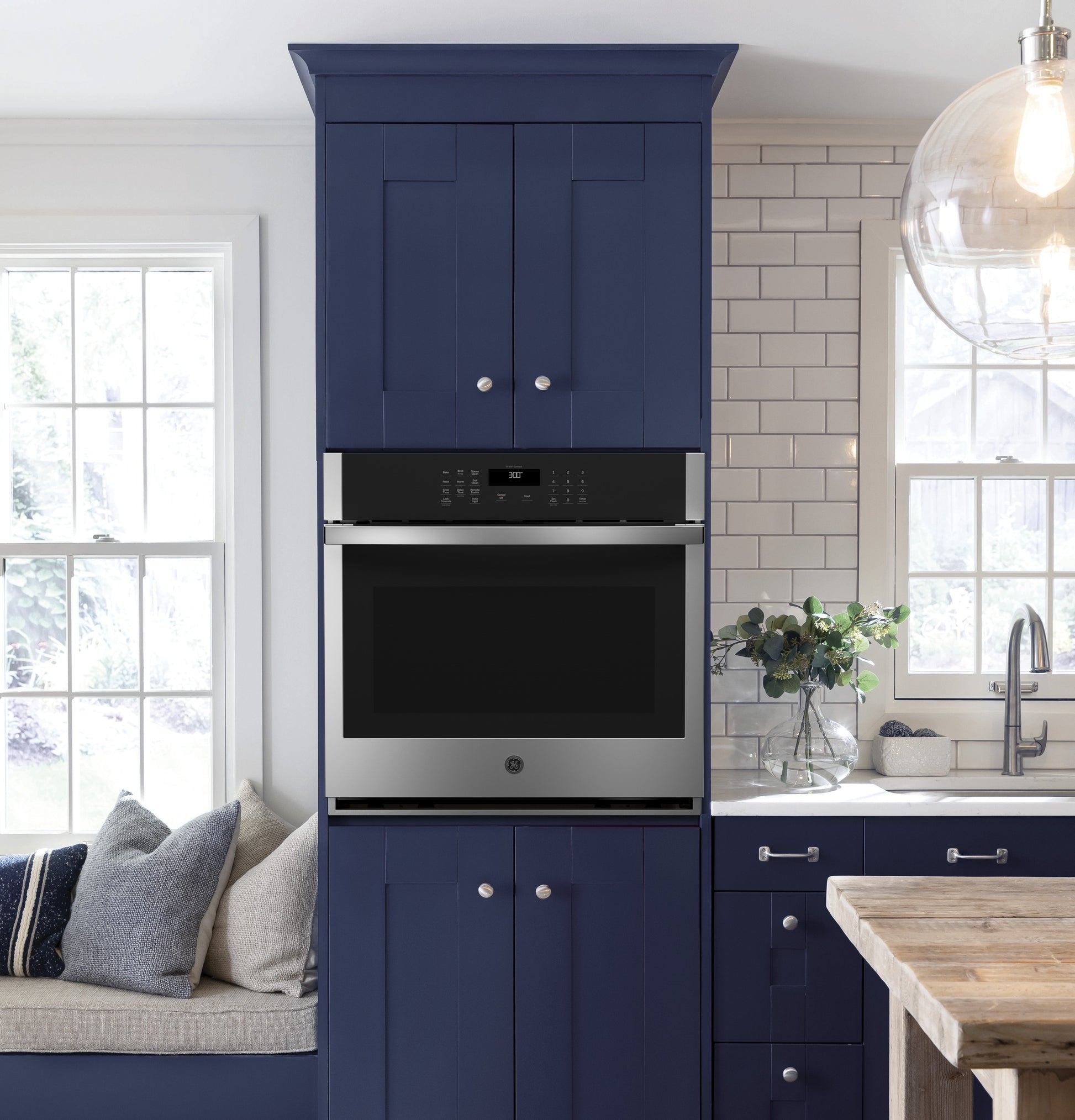 Built-in stainless steel single wall oven installed in blue kitchen cabinetry with white subway tile backsplash
