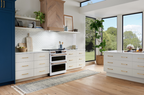 Modern kitchen with white cabinetry, natural wood vent hood, and large windows showcasing greenery from Over the Range Hoods collection