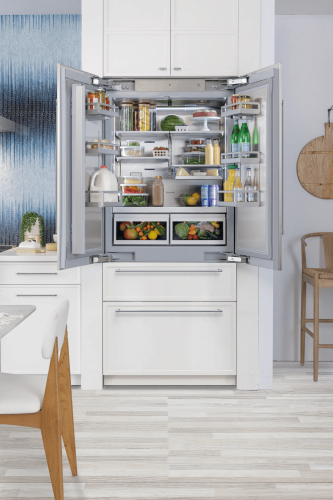 Built-in French door refrigerator open to show organized fresh produce, beverages, and dairy in a modern kitchen setting