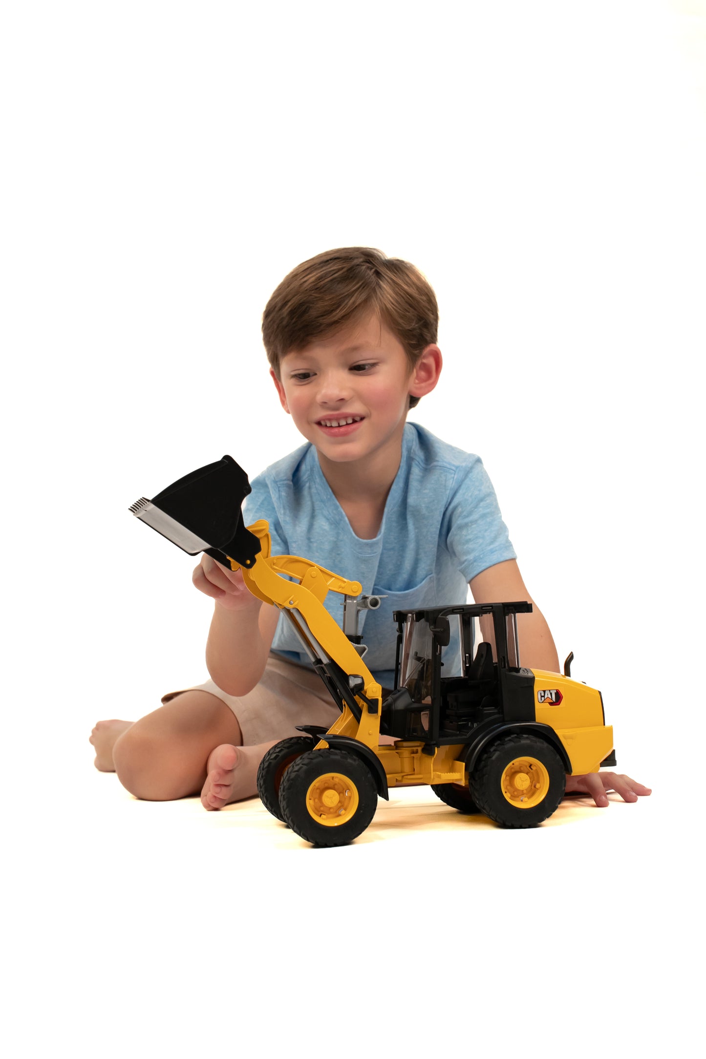 Young boy playing with yellow Bruder construction wheel loader toy in tools and home improvement setting