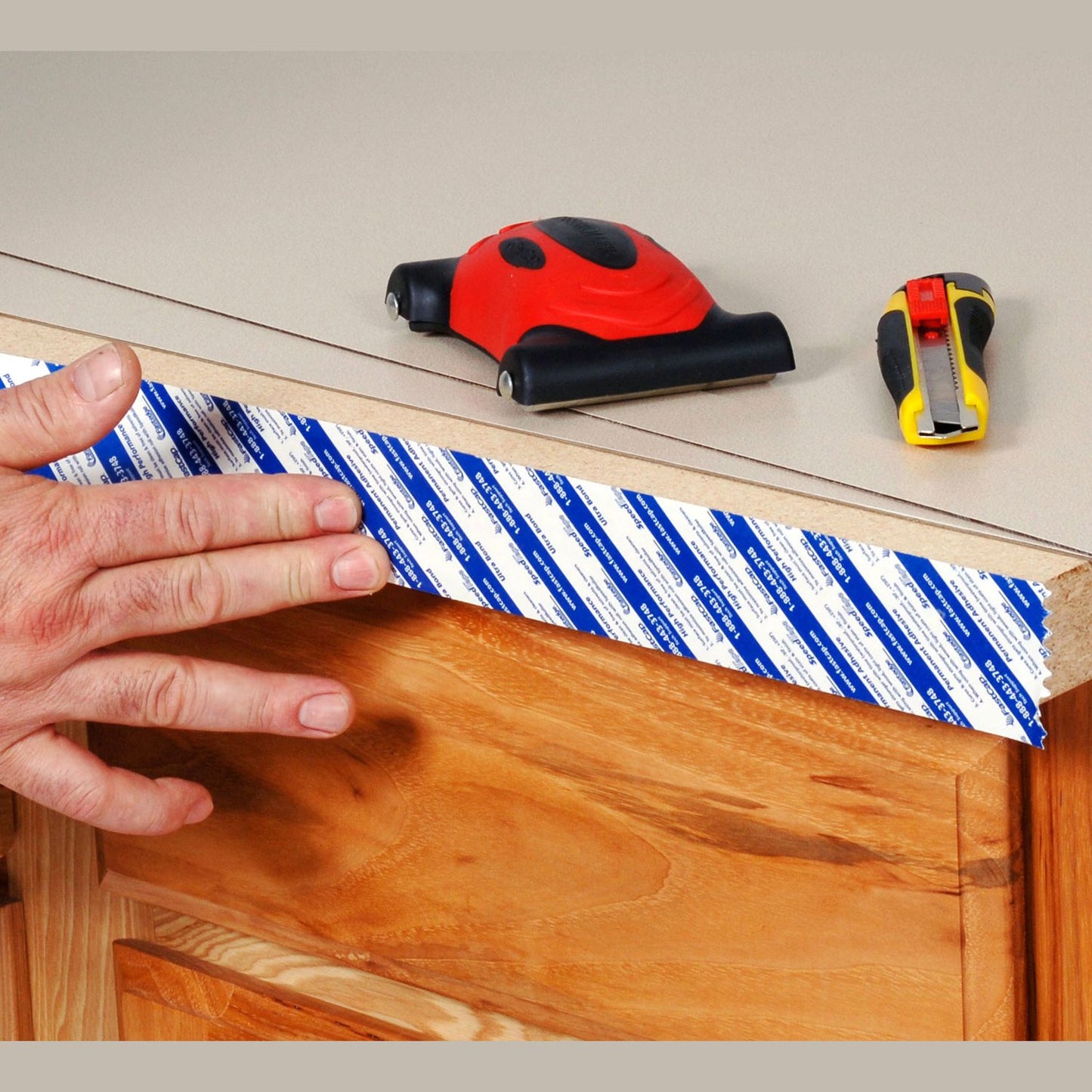 Hand applying blue and white Speedtape adhesive to wood edge with measuring tape and utility knife nearby for woodworking tools