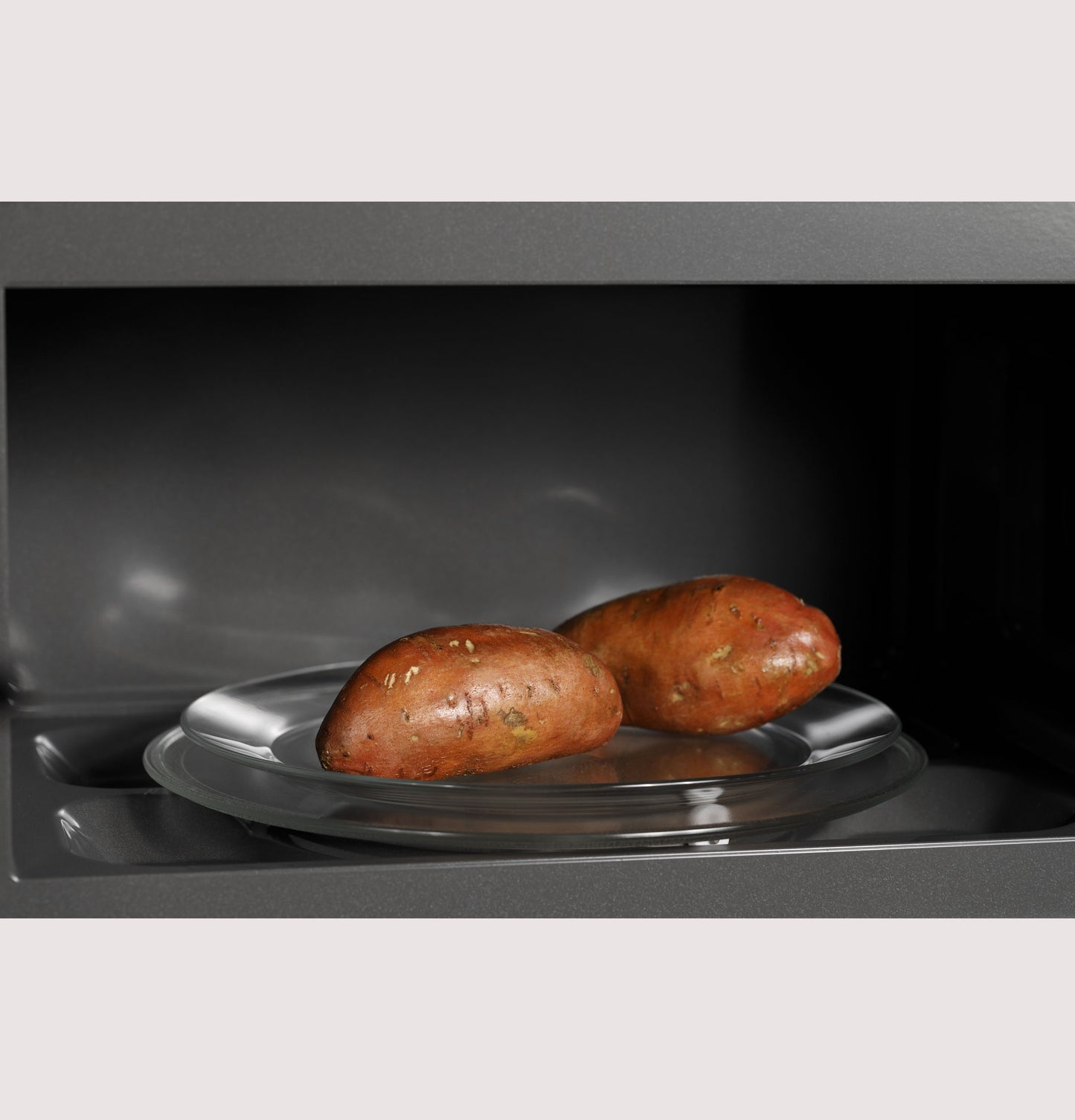 Glass microwave interior with two sweet potatoes on a rotating glass tray from kitchen appliances collection