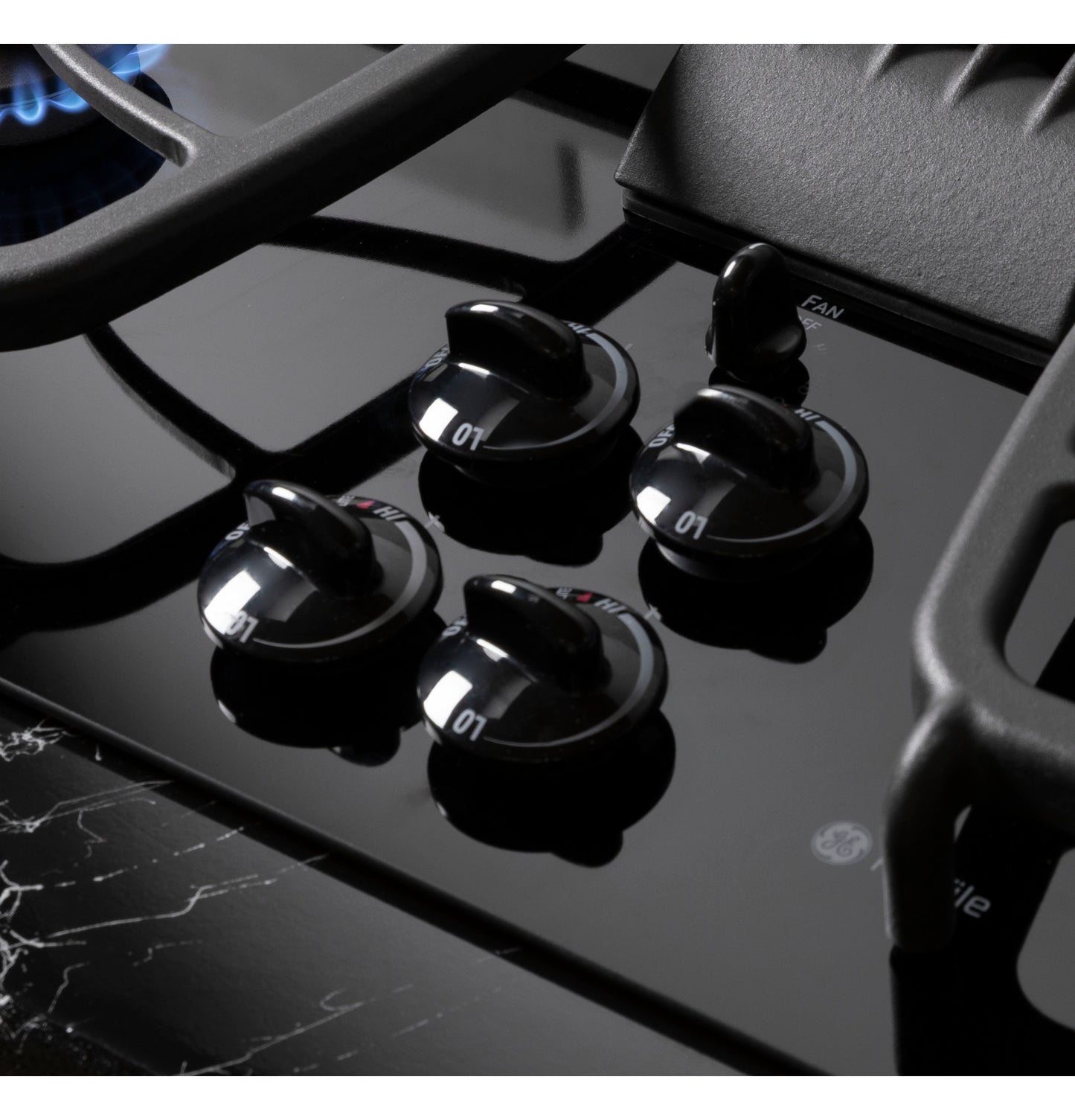 Close-up of glossy black glass gas cooktop surface featuring four sleek control knobs and cast iron grates in kitchenware setting