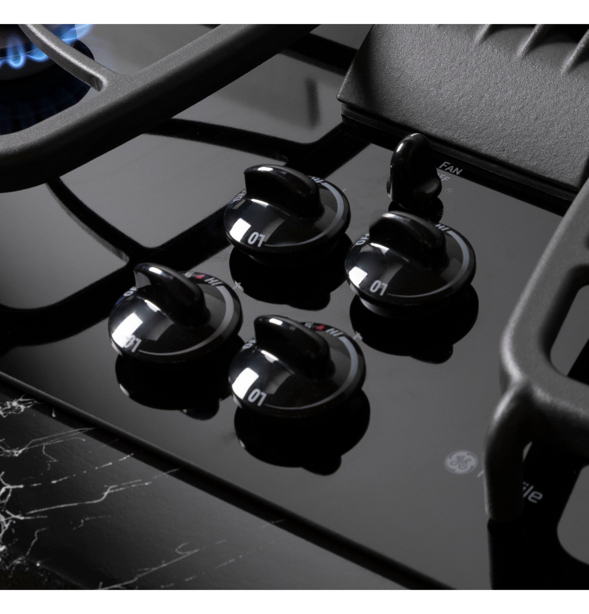 Close-up of glossy black glass gas cooktop surface featuring four sleek control knobs and cast iron grates in kitchenware setting