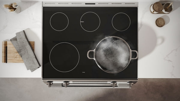 Top view of a black electric induction cooktop with four burners and a boiling pot on a white marble countertop