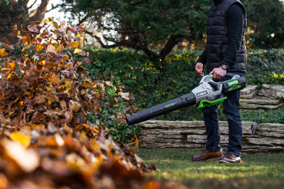 Person using EGO Power+ cordless blower to clear fallen autumn leaves in a backyard setting for home maintenance