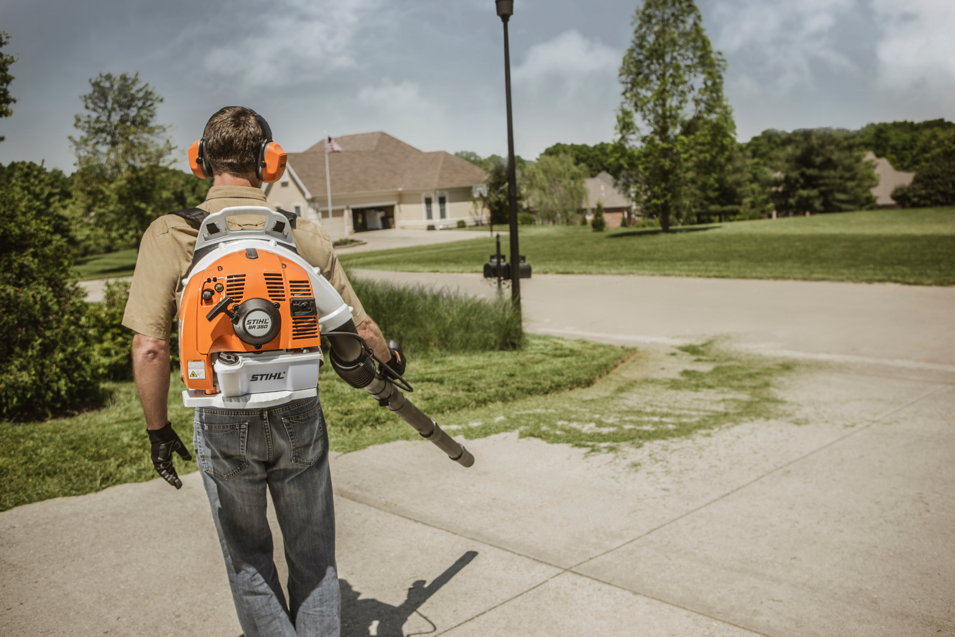 Man wearing ear protection operating orange and white fuel-efficient backpack blower for outdoor yard maintenance tasks