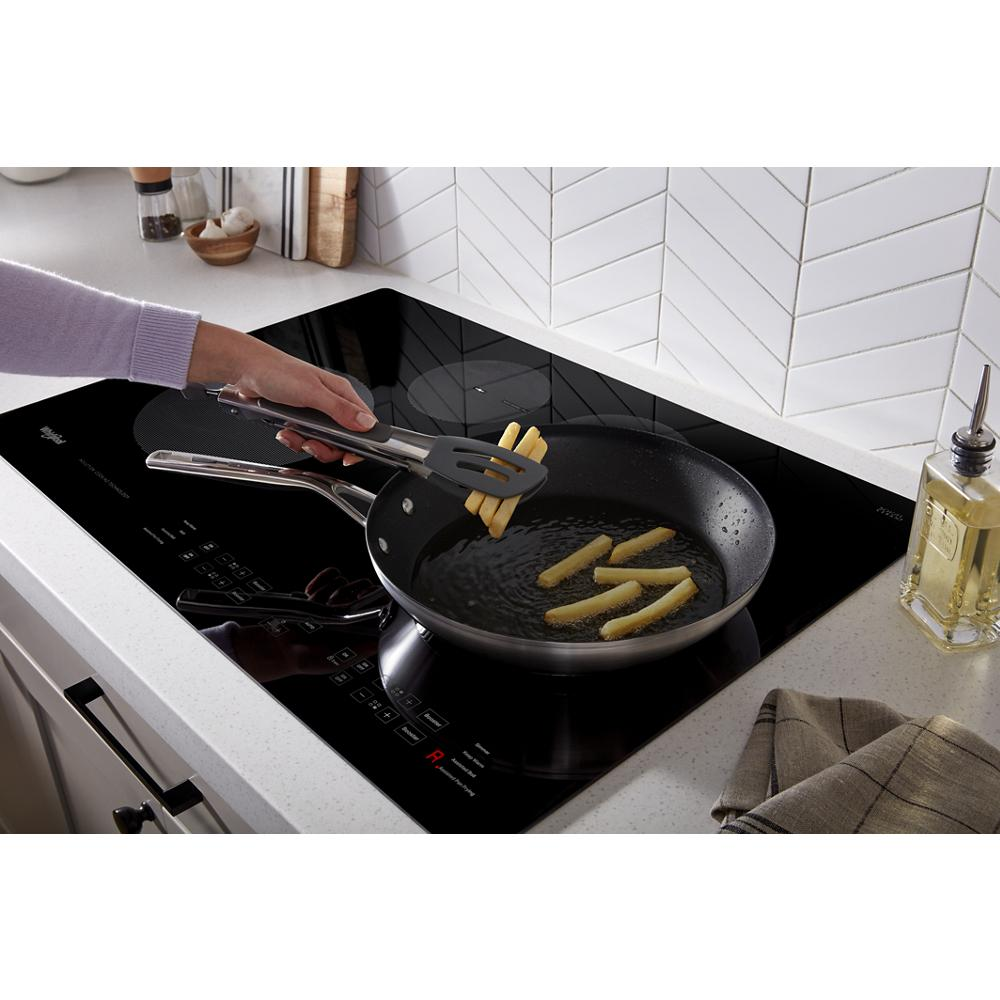 Black 30-inch induction cooktop frying fries in nonstick pan on white countertop with kitchenware and appliances nearby