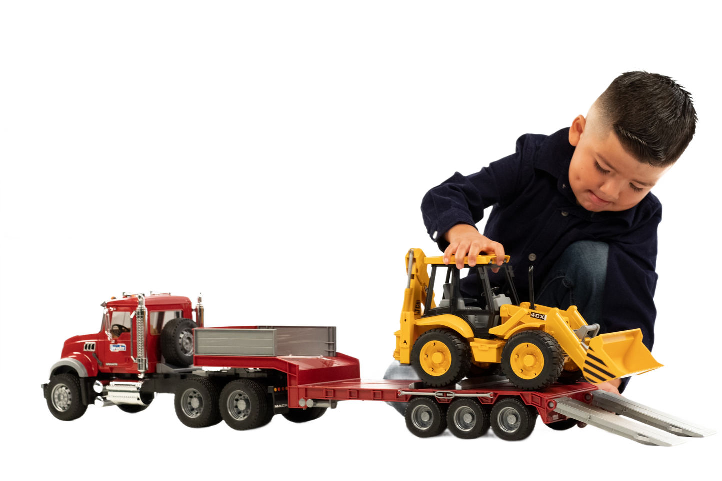 Child playing with red toy truck and yellow backhoe loader on a detachable lowboy trailer for construction play