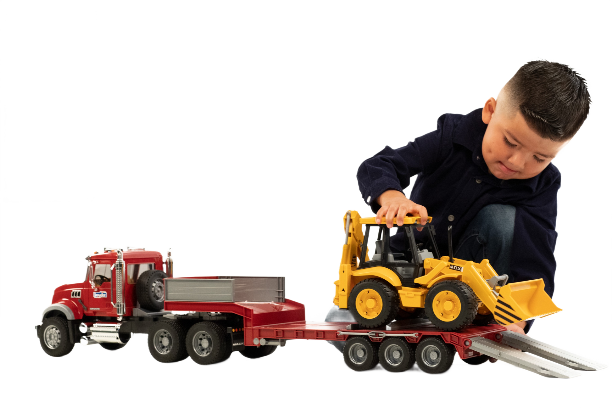 Child playing with red toy truck and yellow backhoe loader on a detachable lowboy trailer for construction play