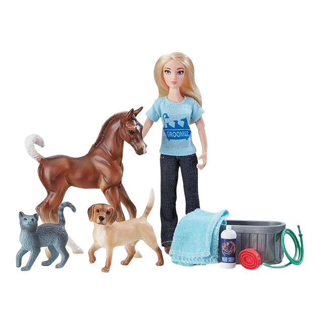 Doll wearing blue grooming shirt with horse, dog, cat figures, towel, shampoo bottle, bucket, and hose toy set
