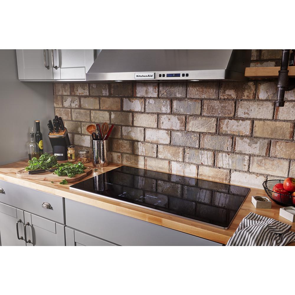 Black glass electric cooktop with five touch controls installed in kitchen with butcher block countertop and brick wall backsplash