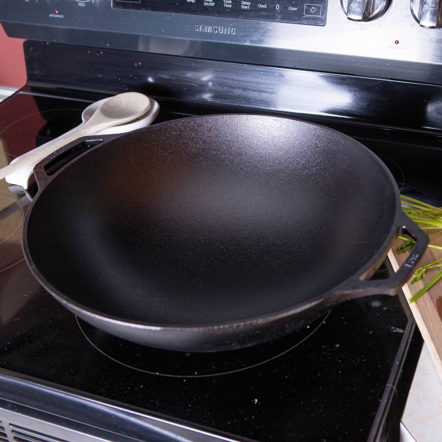 Black cast iron wok with wide base and dual handles set on electric stovetop for kitchenware collections under $100