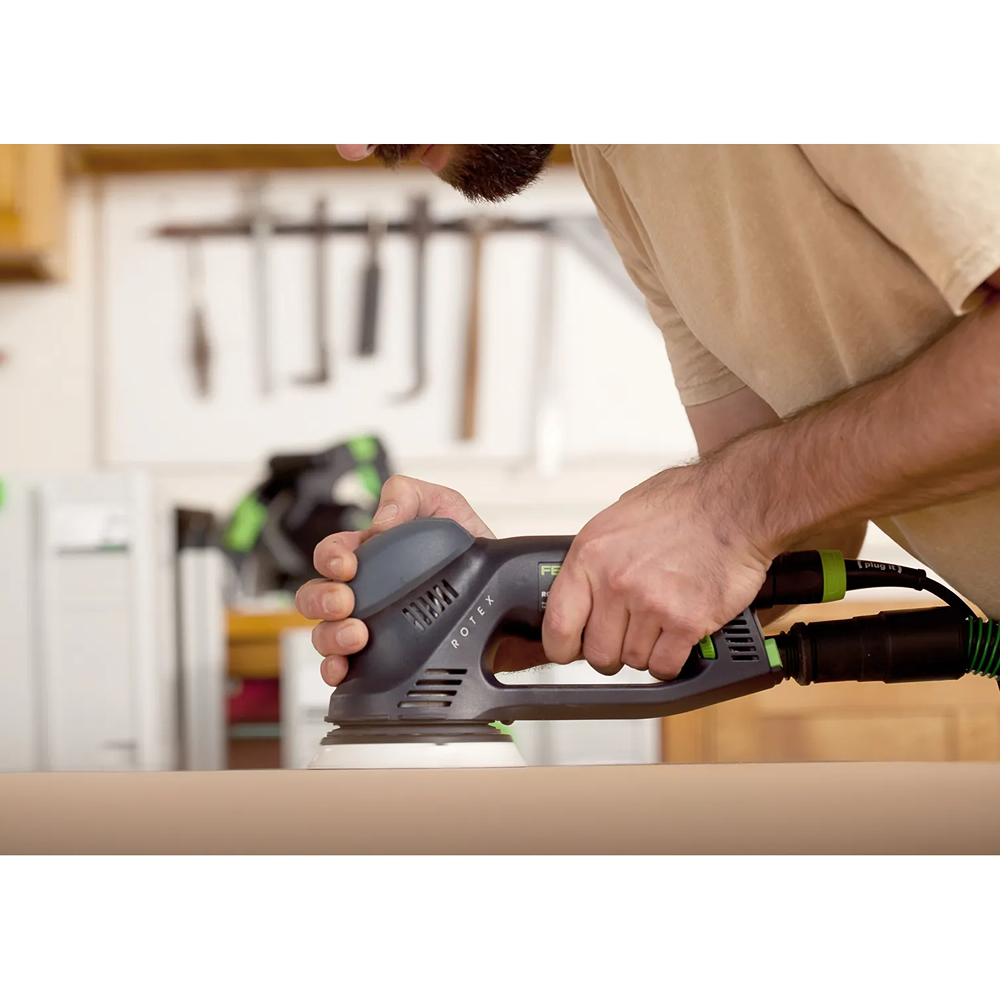 Person using a Festool Rotex dual mode sander with dust extraction on wood surface in a home improvement workshop