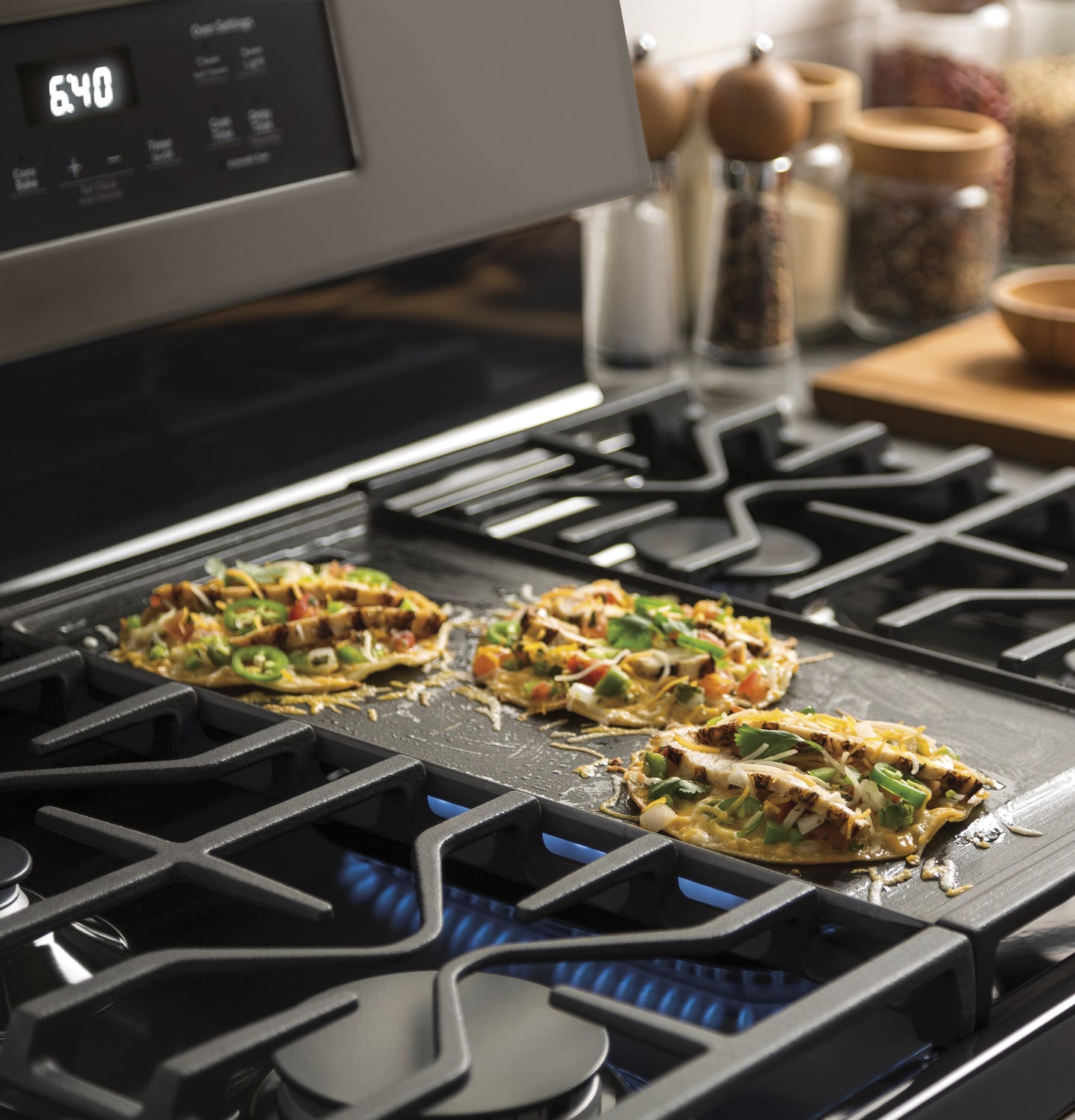 Close-up of three mini quesadillas cooking on a black griddle over a gas range burner in a kitchen setting