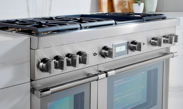 Stainless steel dual fuel range with digital display, six burner grates, and double oven doors in modern kitchen setting