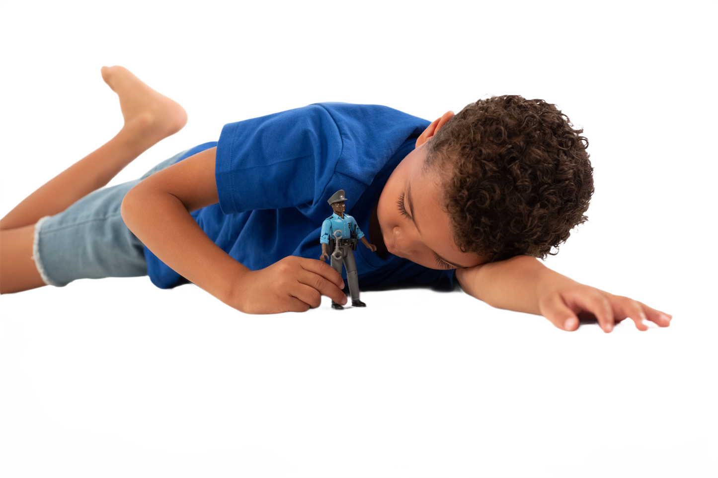 Child lying down closely observing a dark-skinned policeman toy figure with detailed blue uniform and accessories