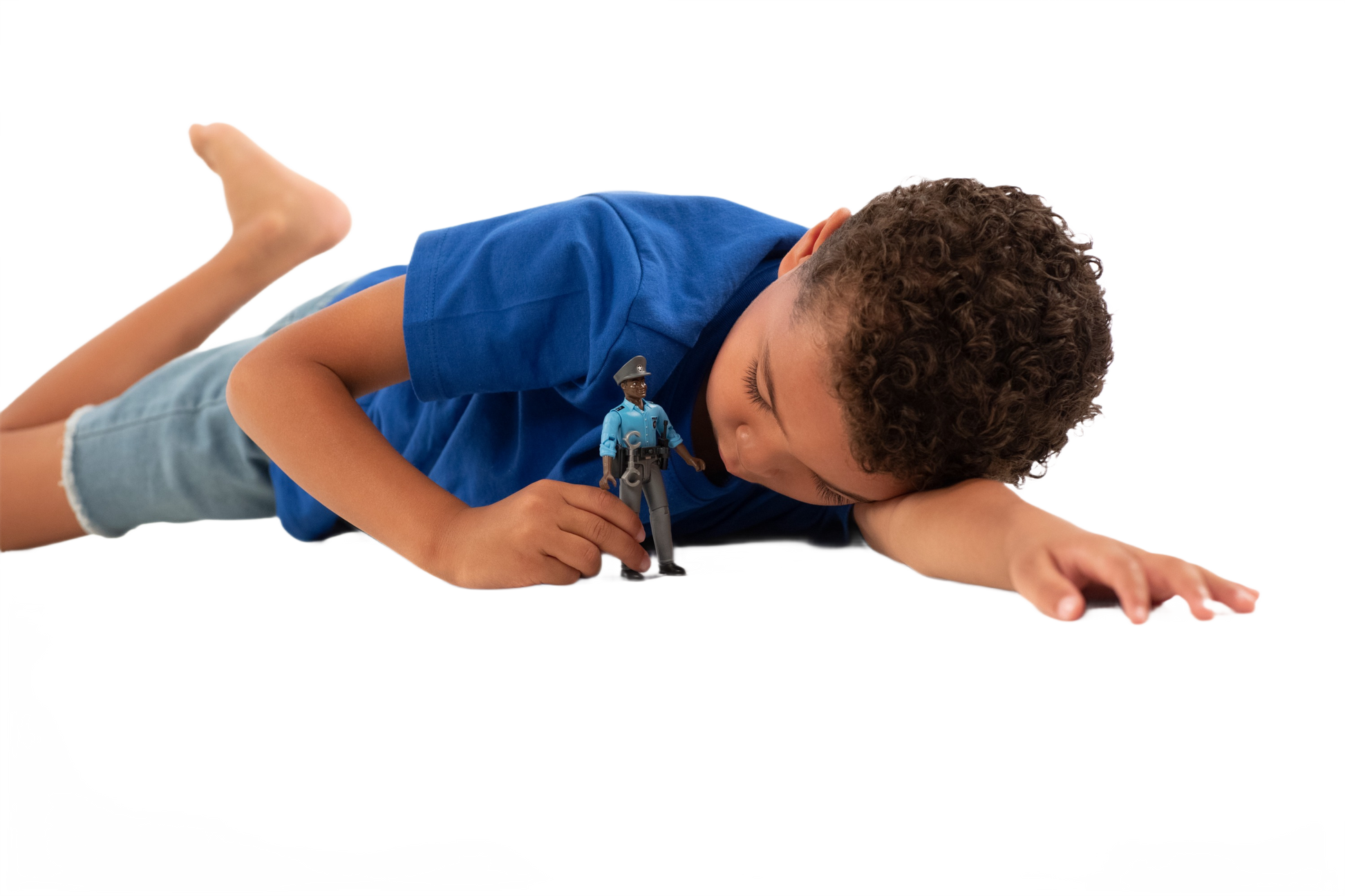 Child lying down closely observing a dark-skinned policeman toy figure with detailed blue uniform and accessories