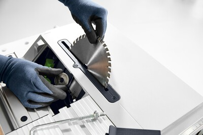 Person wearing gloves installing a circular saw blade on a Festool cordless table saw in a workshop