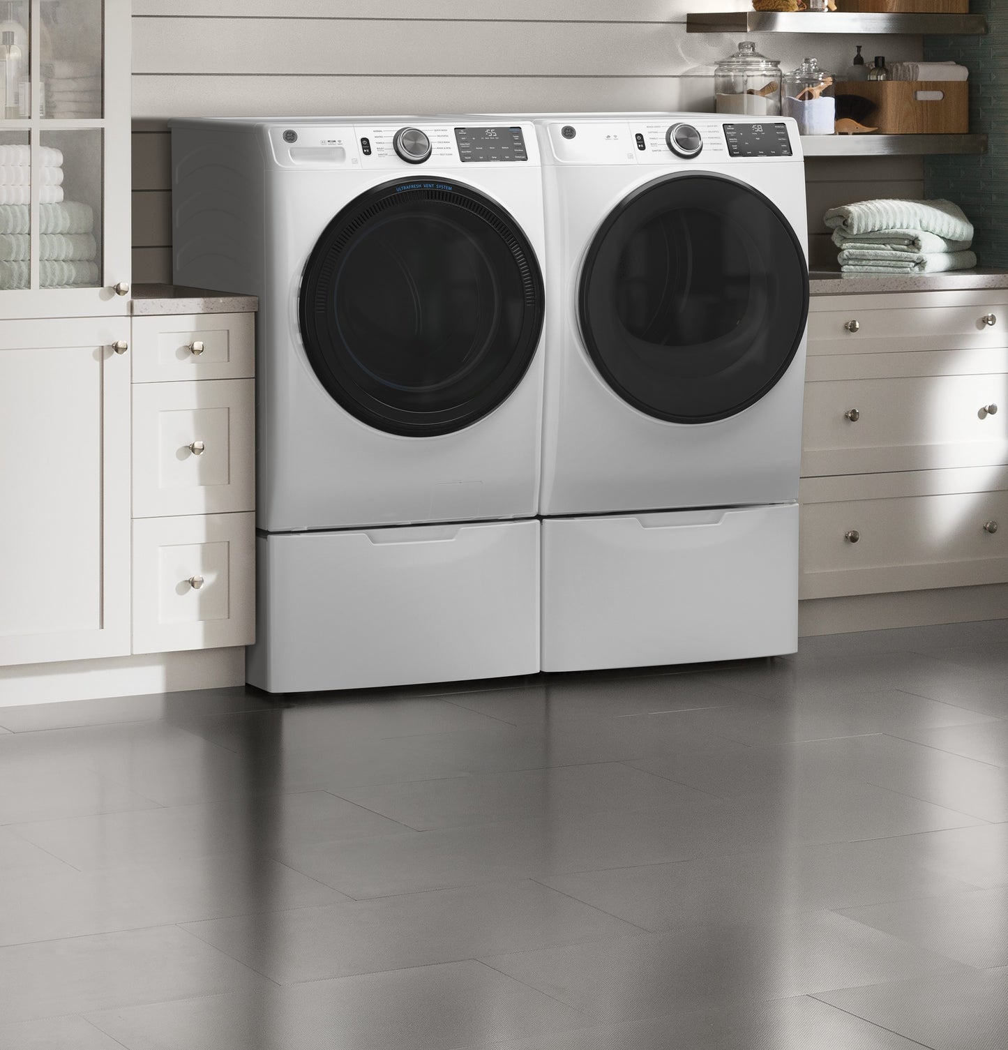 Pair of white smart front load electric washer and dryer with pedestal bases in a modern laundry room from appliances collection