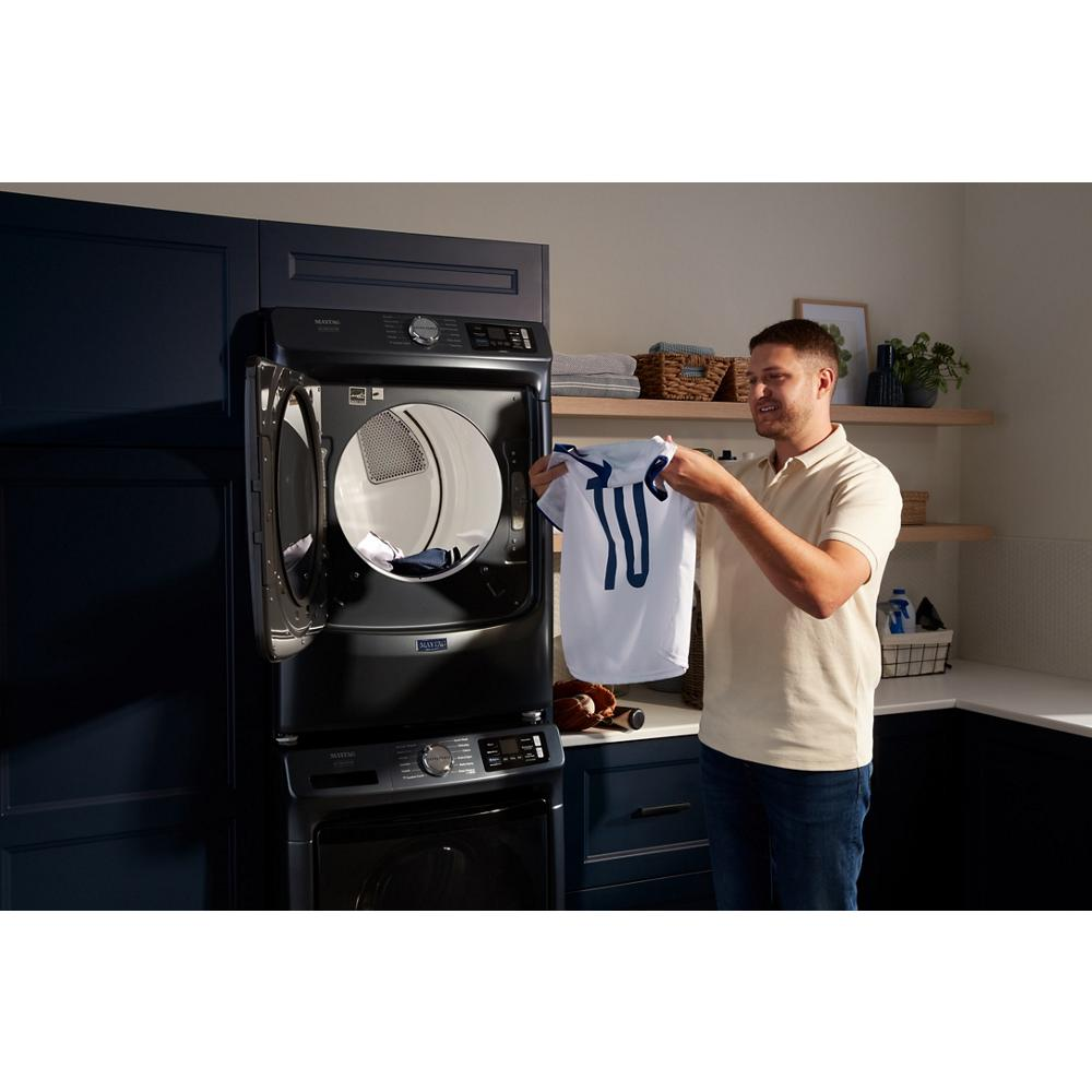 Man holding a white and blue sports jersey by a dark front load washer in modern laundry room with shelves and towels