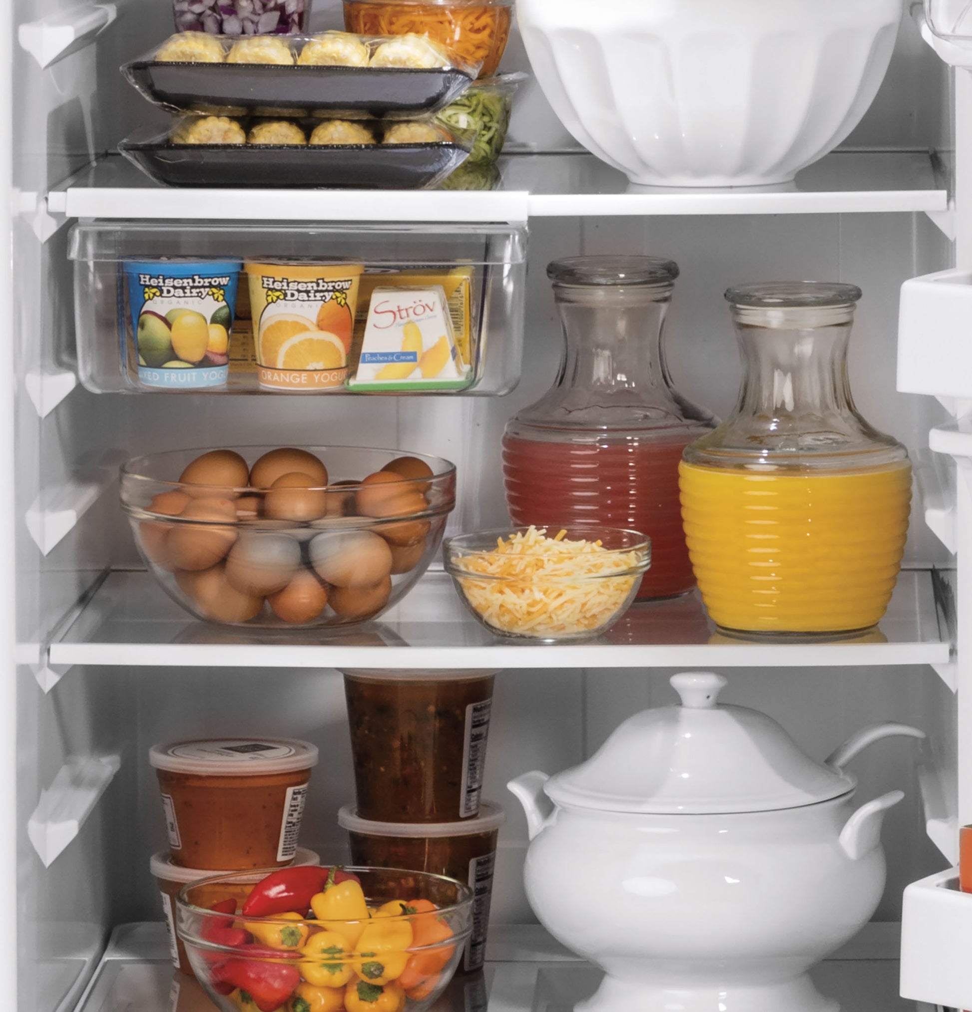 Open refrigerator shelves filled with eggs, juice pitchers, shredded cheese, and clear containers in kitchen appliances collection