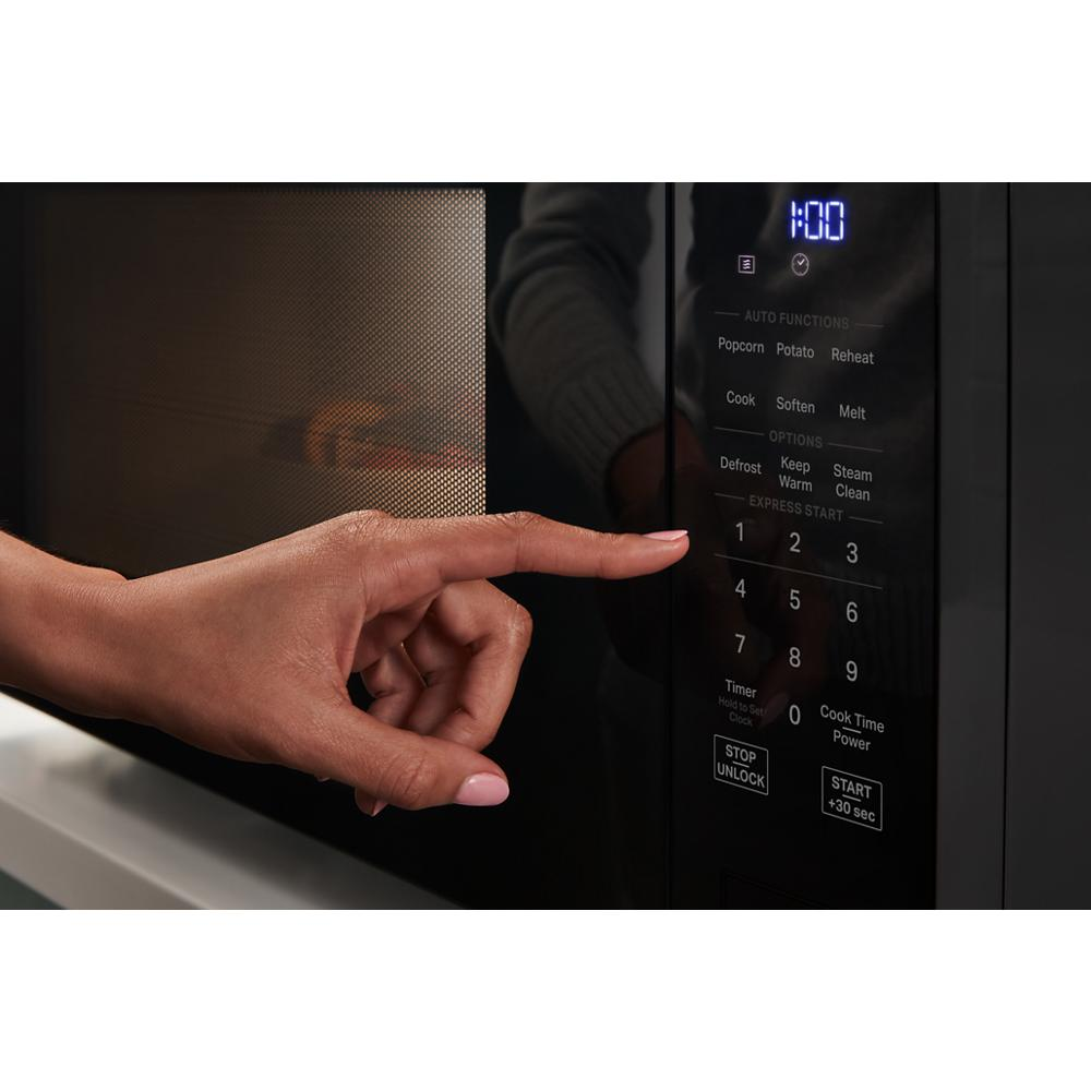 Hand pressing digital control panel on black sensor cooking microwave in modern kitchen appliance setting
