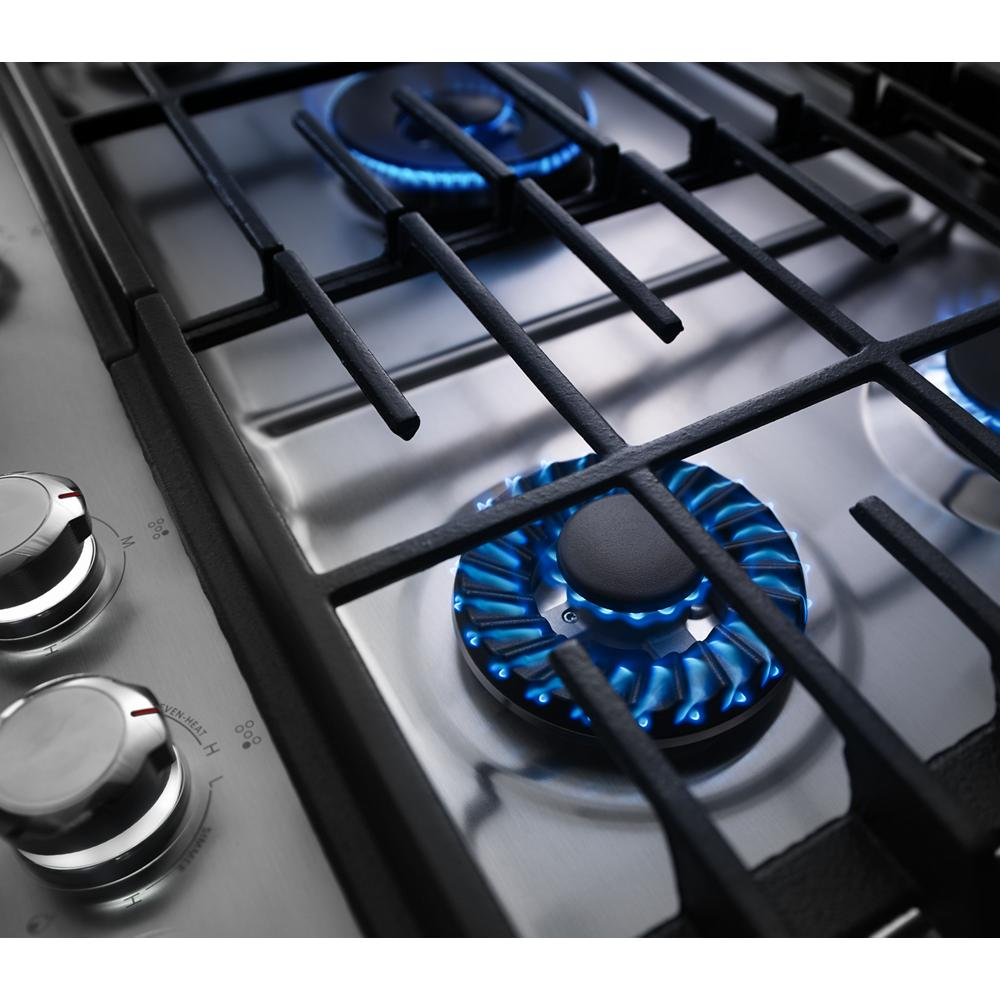 Blue flames burning on a stainless steel gas cooktop burner with black cast iron grates in KitchenAid cooktop collection