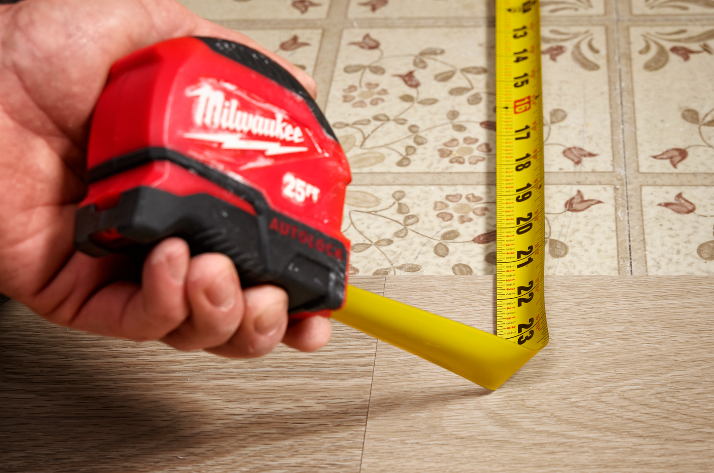 Red and black Milwaukee 25-foot auto-lock tape measure extending on tiled floor for home improvement tools