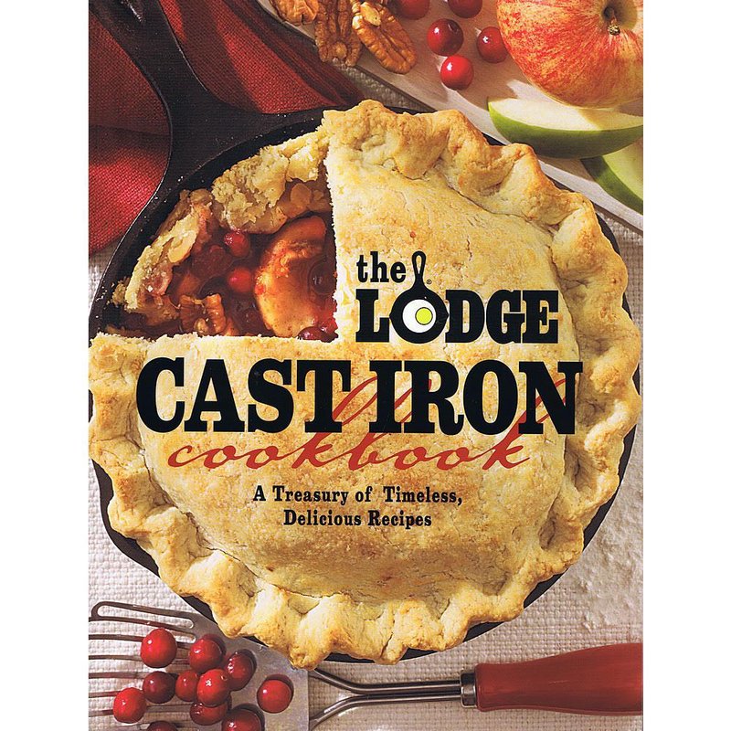 Freshly baked fruit pie with nuts and cranberries in a cast iron skillet alongside apples and kitchen utensils