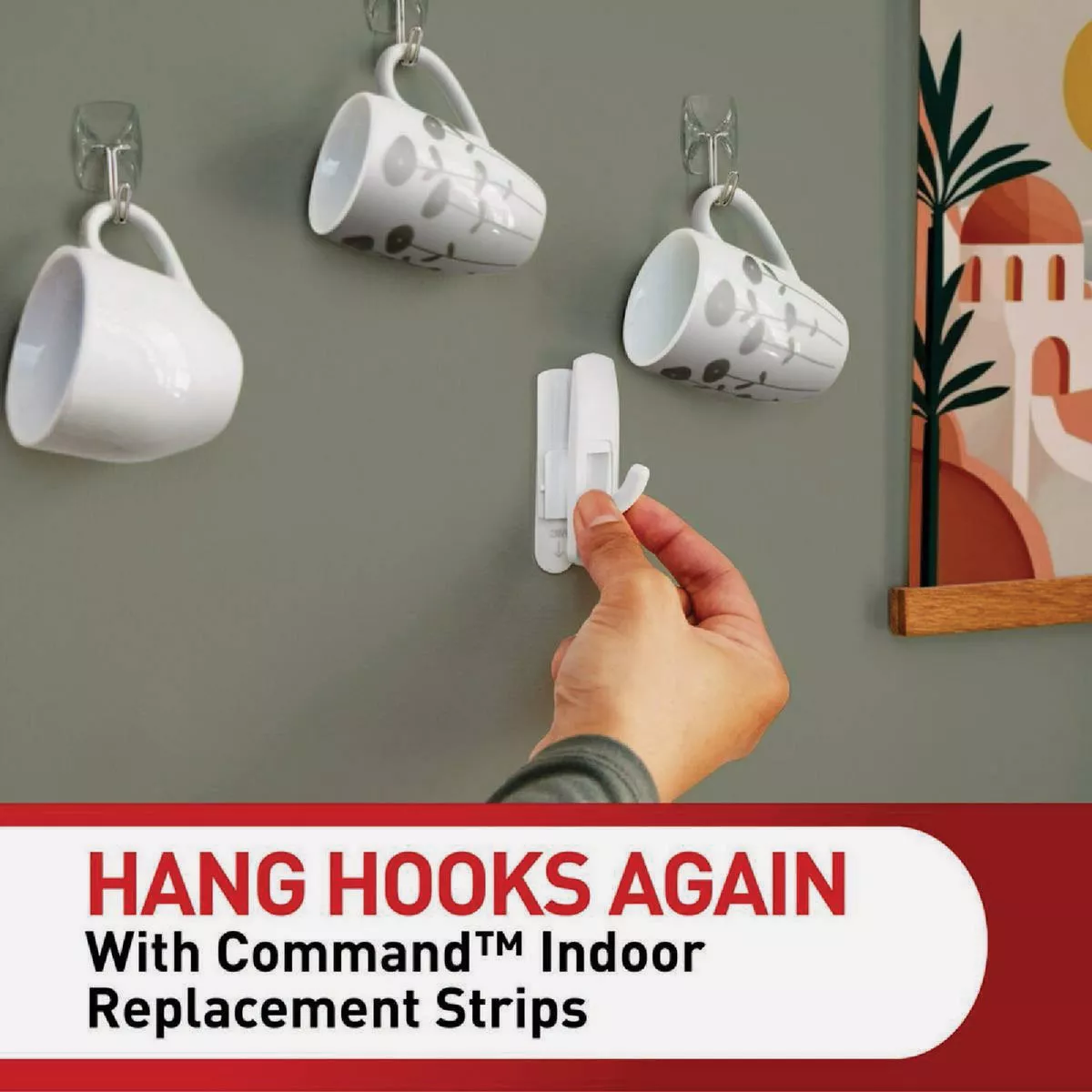 Hand attaching a white indoor adhesive hook to gray wall with cups hanging using damage-free fasteners in home hardware setting