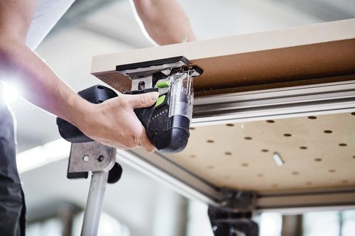 Person cutting wood panel with Festool cordless barrel grip jigsaw on workbench in power tools setting